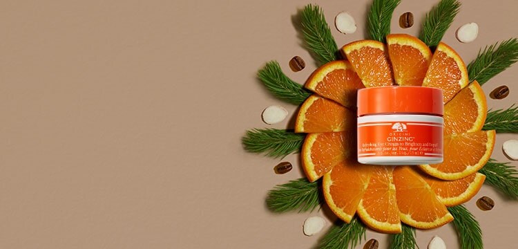 Origins GinZing Eye Cream laid on top of slices of orange, ginseng and coffee beans. 